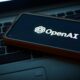 smartphone on laptop keyboard showing OpenAI logo