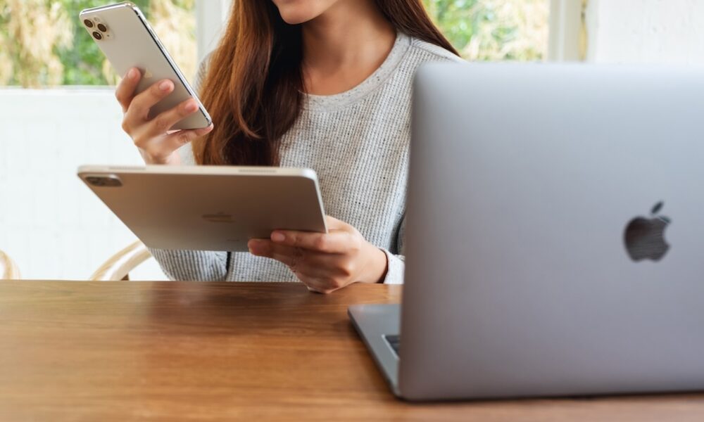Jun 16th 2020 : An asian woman holding and using Iphone 11 Pro Max smart phone and Apple New Ipad Pro 2020 tablet pc with Apple MacBook Pro laptop computer on wooden table , Chiang mai Thailand