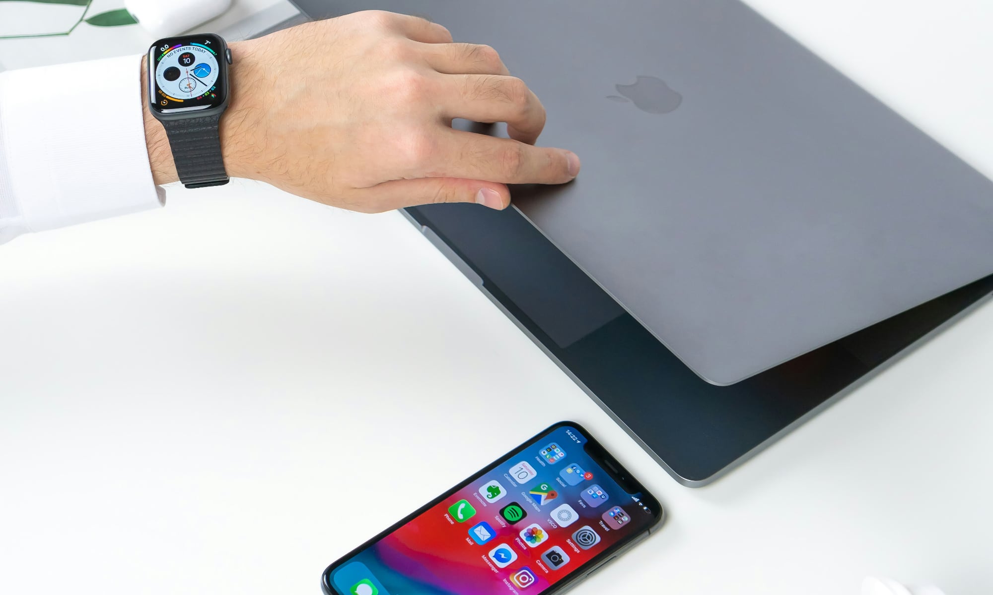 person opening MacBook wearing Apple Watch with iPhone