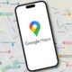 Google Maps logo with lettering is displayed on a smartphone lying on a map view of Google Maps
