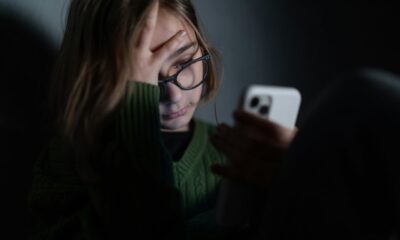 A sad girl alone in darkness sitting and using an iPhone