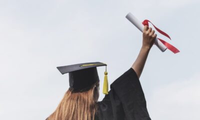 Rear view of woman in a cap and gown holding a diploma in the air.