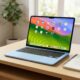A concept image of a colorful 12.9-inch budget MacBook in pastel blue sitting on a wooden desk in a sunlit student room.