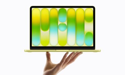 Citrus MacBook Neo beind held up on top of a hand.