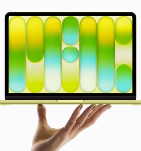 Citrus MacBook Neo beind held up on top of a hand.