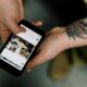 tatooed man holding iphone and scrolling through social media