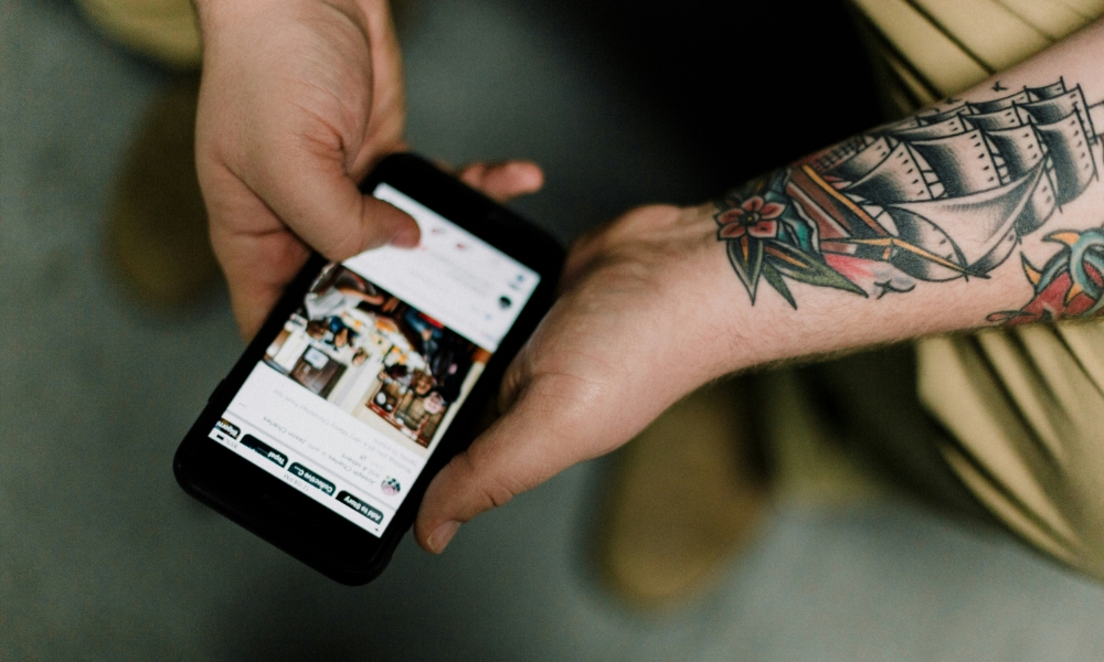 tatooed man holding iphone and scrolling through social media