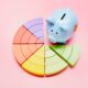 High angle view of a piggy bank and colorful pie chart on pink background; cash flow analysis