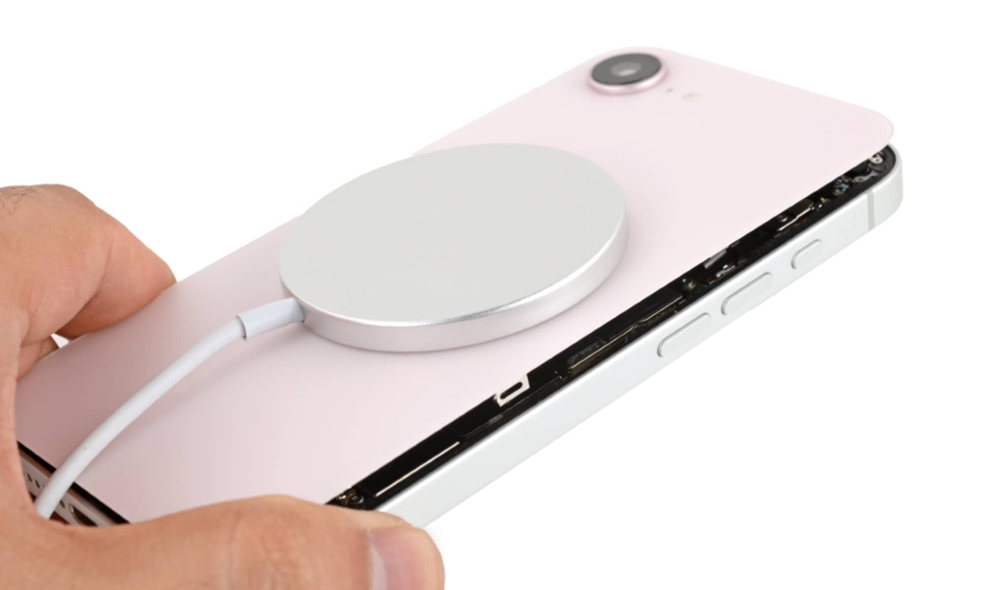 Person holding an iPhone 16e with a soft pink iPhone 17e glass back with a MagSafe charger attached to it.