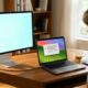 A sleek 2026 Apple Studio Display sits on a modern wooden desk next to an older MacBook Pro in a bright, sunlit home office.
