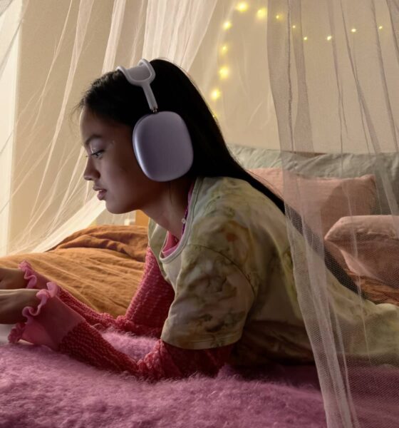 Girl laying on bed using a MacBook Neo while wearing AirPods Max.