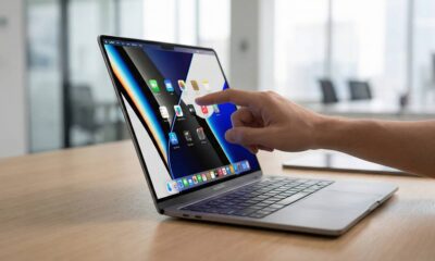 A close-up lifestyle concept shot of a person’s hand using touch gestures on the ultra-slim OLED display of a 2026 MacBook Pro in a bright, modern office setting.