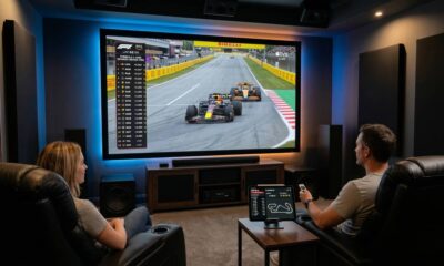 A modern living room in 2026 showcasing a huge screen displaying a Formula 1 race on Apple TV in 4K. An iPad Pro with the Apple Sports app is open on the coffee table nearby.