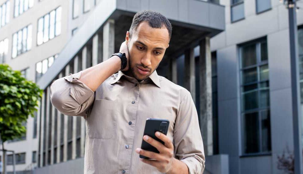Dunkelhäutiger Mann blickt ratlos auf sein Handy