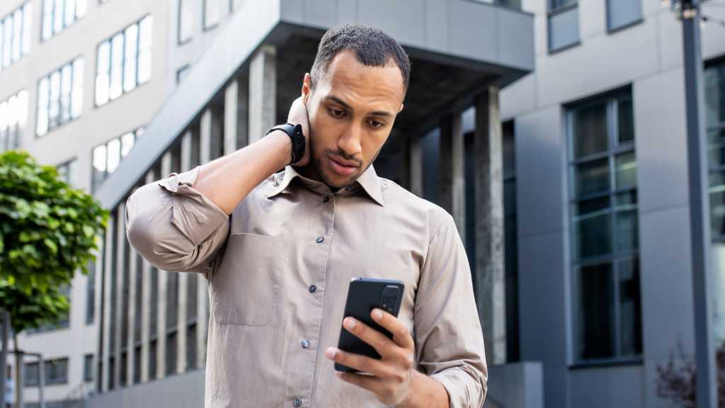 Dunkelhäutiger Mann blickt ratlos auf sein Handy