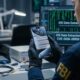 A focused photograph from an over-the-shoulder perspective of an FBI forensic specialist in 2026, wearing an official patch and nitrile gloves. They are holding a modern iPhone in a dimly lit tech lab. The iPhone screen is the central focus, displaying multiple notifications with message previews that reveal private Signal conversations. The background is a detailed, slightly blurred lab environment with diagnostic equipment and computer monitors showing data analysis.