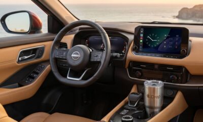View from inside a premium car interior at sunset. The central dashboard display shows Apple CarPlay with sports score widgets active.