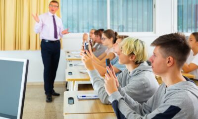 Teen students using social media on phones on lesson