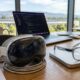 A high-end workspace featuring a dusty Apple Vision Pro M5 headset sitting next to a pair of sleek, prototype-style AR smart glasses on a charging pad.