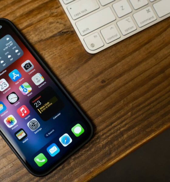 An iPhone sitting next to a Magic Keyboard on a wooden table.
