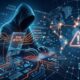 A conceptual digital illustration of a hooded hacker sitting at a glowing keyboard, surrounded by a dark blue and orange network grid showing a global map, a large warning triangle icon, and floating holographic text overlays that read "Scam Detected," "AI Voice Generation," and "Phishing Link."