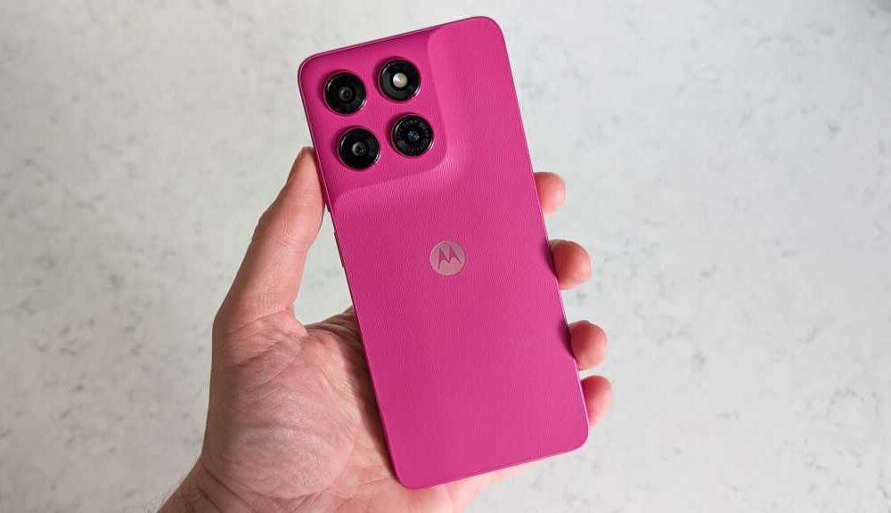 A hand holding a pink smartphone, with the rear of the handset facing the camera