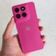 A hand holding a pink smartphone, with the rear of the handset facing the camera
