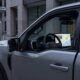 A conceptual hero image of the future Ford UEV $30,000 mid-size electric truck, parked in a futuristic charging plaza, with a screen showing Apple Maps integrated navigation.