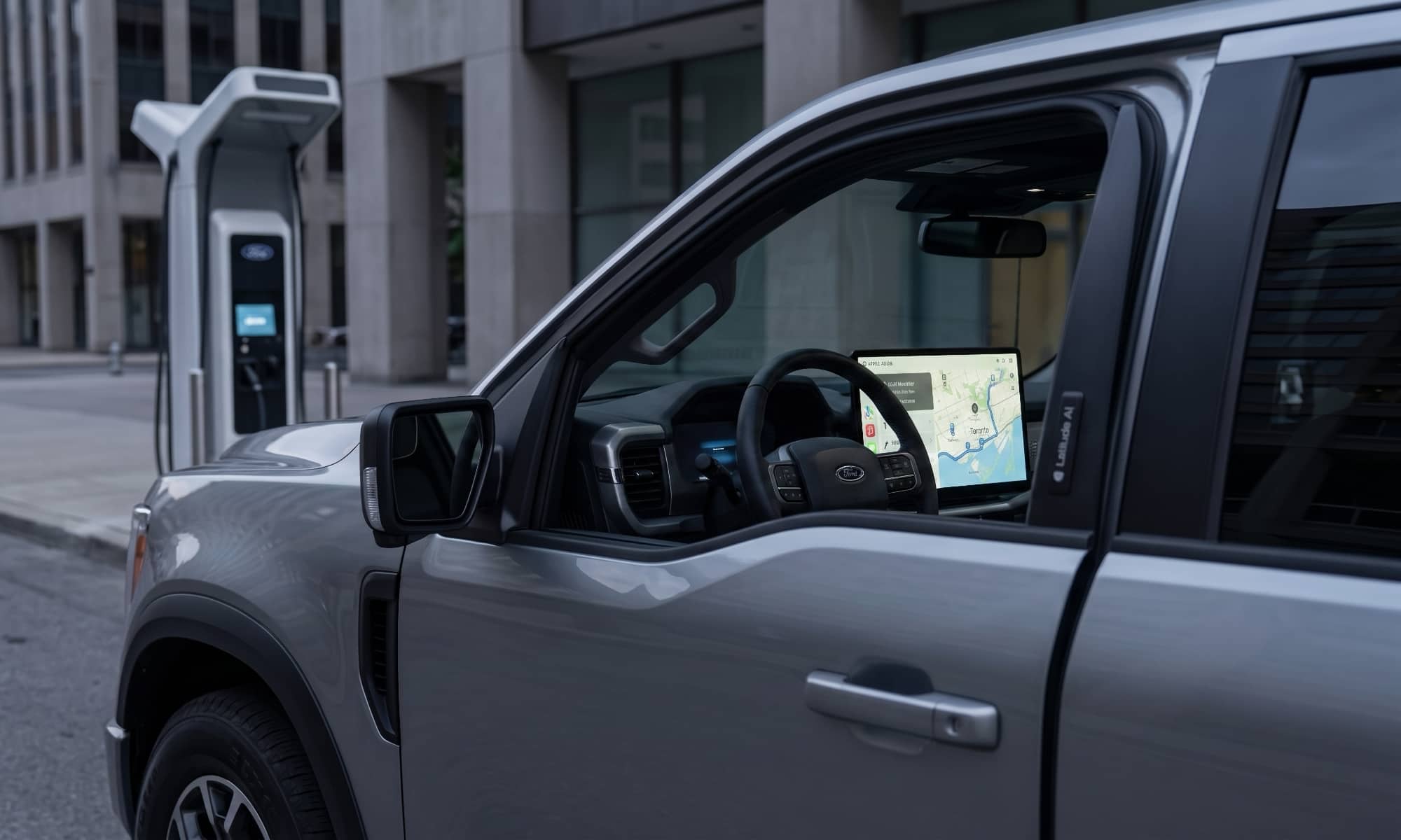 A conceptual hero image of the future Ford UEV $30,000 mid-size electric truck, parked in a futuristic charging plaza, with a screen showing Apple Maps integrated navigation.