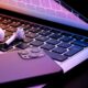 a laptop half closed in the dark with a phone and wireless earphones glowing
