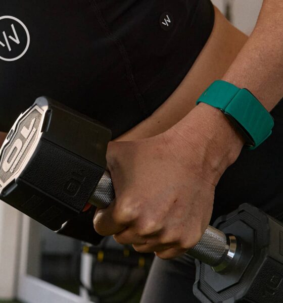 Woman wearing green Whoop fitness band while lifting weights.