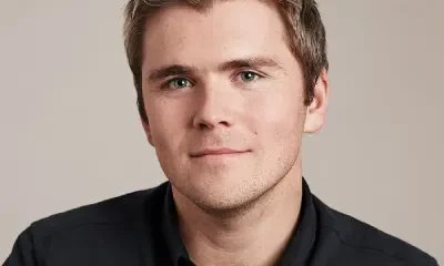 Headshot of Stripe co-founder and President John Collison, wearing a dark collared shirt against a light gray background.