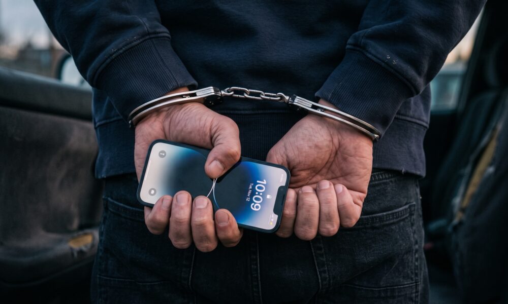 A person handcuffed behind their back holding an iPhone.