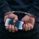 A person handcuffed behind their back holding an iPhone.